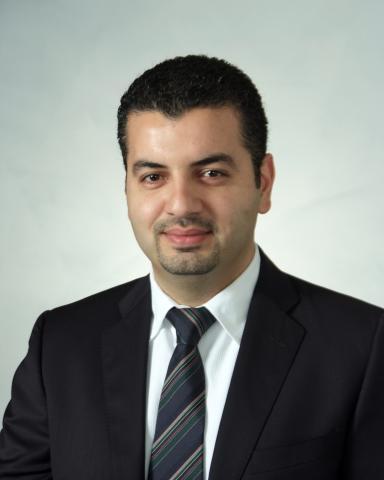 Headshot of Elie Abu Jawdeh, MD, PhD. He's has short dark hair, a bit of a widow's peak, and a faint mustache and goatee. He's wearing a dark suit with a white collared shirt and a dark tie with subtle diagonal stripes. 