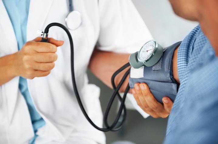 Image of someone in a white coat taking someone else's blood pressure. The photo is zoomed in on the blood pressure cuff and doctor's hands, so we can't see their faces. 