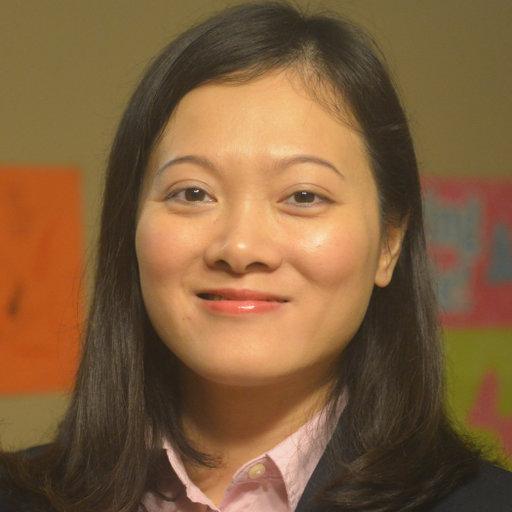 Headshot of a young asian woman with shoulder-length, straight black hair; she's smiling at the camera and wearing a dark coat jacket with light pink collared shirt. Behind her is a tan wall. 