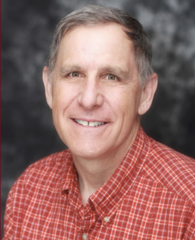 Headshot of Headshot of Milton Eder, an older white man with short gray-brown hair and a soft smile. He's wearing a red plaid button-up shirt and there's a marbly gray backdrop behind him. 